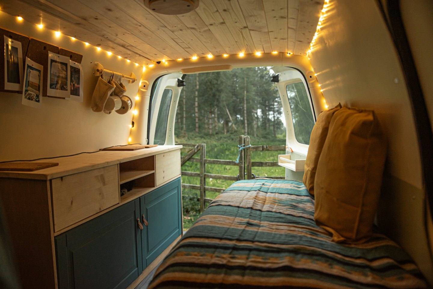 Cozy camper van interior with forest view through open doors.