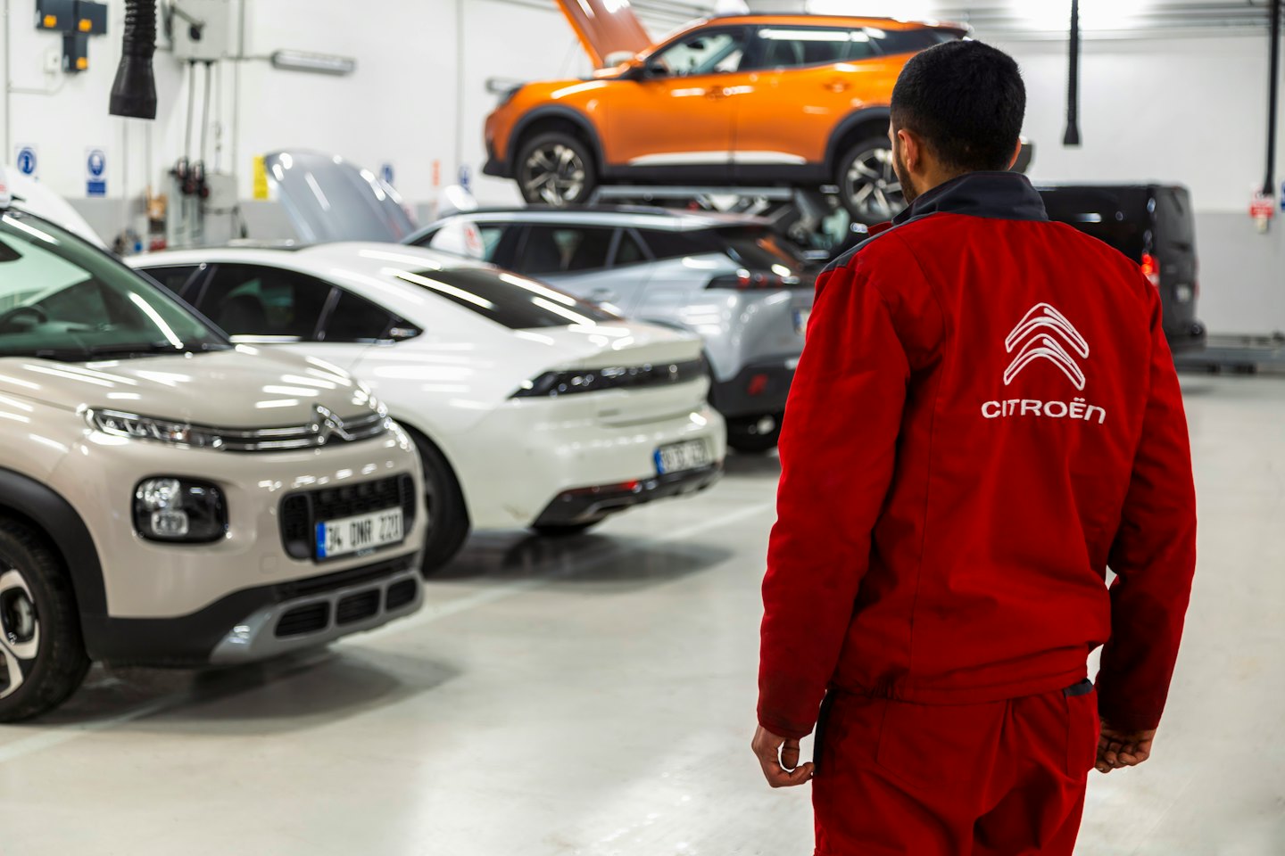 Mechanic in red uniform looking at cars in workshop.